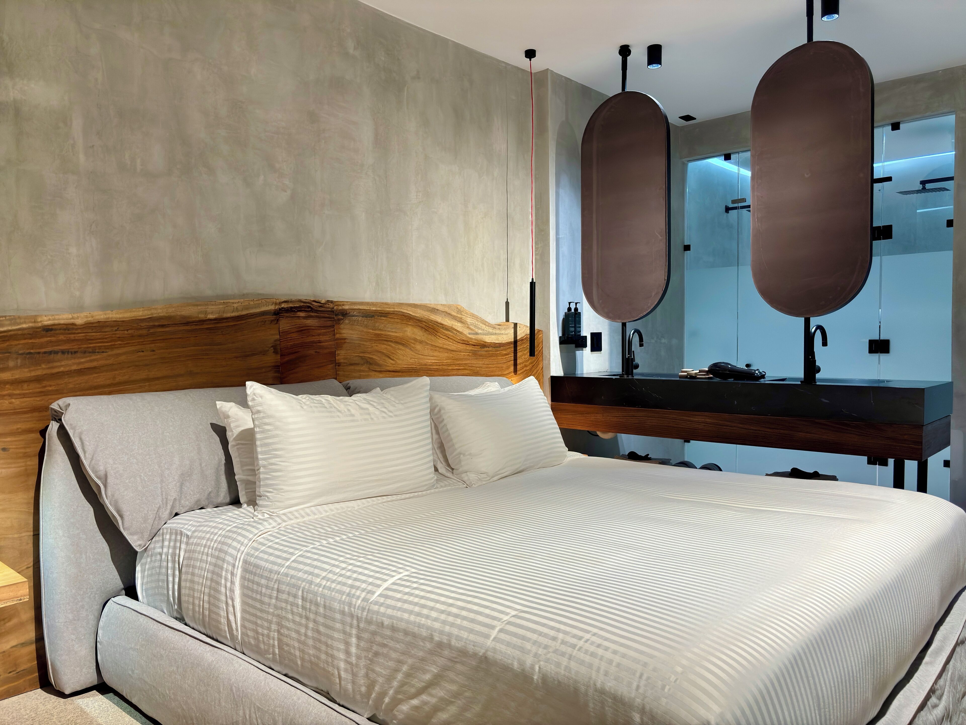 Una camera da letto moderna con una testiera in legno, un letto grande con biancheria da letto bianca, un comodino e uno specchio integrato sopra il mobile da trucco.