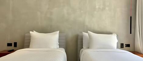 A hotel room with two beds, each with white linens and pillows, against a textured wall.