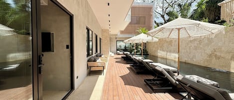 Un espace piscine extérieur moderne, doté d’une terrasse en bois, de chaises longues et de parasols.