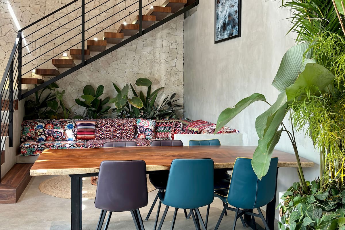 Un intérieur moderne avec une table à manger en bois, des chaises bleues, un canapé coloré et un escalier avec des marches en bois.
