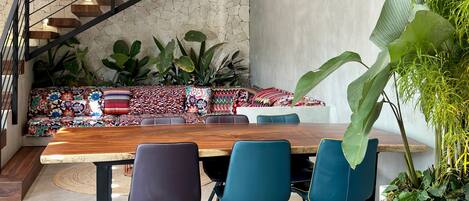 A modern interior with a wooden dining table, blue chairs, a colorful sofa, and a staircase with wooden steps.