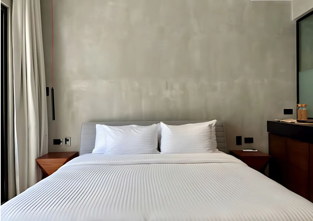 Una habitación de hotel moderna con una cama grande, una mesita de noche de madera, una pequeña mesa y un espejo.