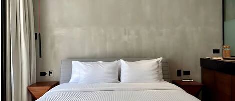 Una habitación de hotel moderna con una cama grande, una mesita de noche de madera, una pequeña mesa y un espejo.