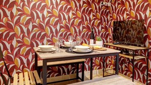 A dining area with a table set for two, a television, and a patterned wall in the background. - TheBlueStay 143 - Superb cozy studio apartment (Paris)