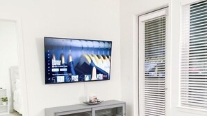 A modern living room with a flat-screen TV mounted on the wall, a grey entertainment unit, a glass coffee table, and a blue sofa. - *New* *Modern* Less than 2 Miles from Universal, Epic Univ, Volcano Bay & More (Orlando)