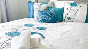 A neatly made bed with a floral-patterned bedspread, two rolled towels, and a wooden headboard. - *New* *Modern* Less than 2 Miles from Universal, Epic Univ, Volcano Bay & More (Orlando)