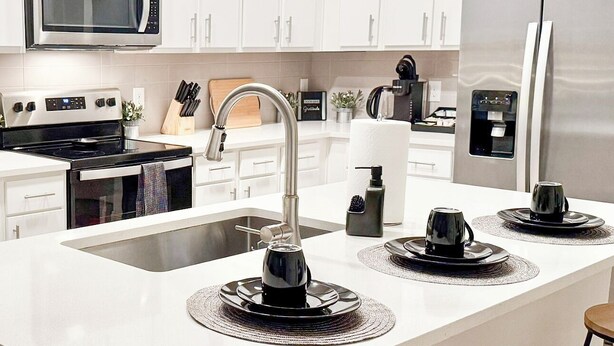A modern kitchen with white cabinetry, stainless steel appliances, a large island with bar stools, and pendant lighting. - *New* *Modern* Less than 2 Miles from Universal, Epic Univ, Volcano Bay & More (Orlando)