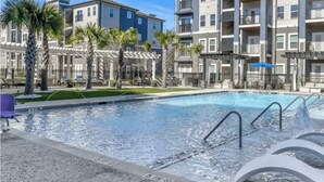 A swimming pool with water fountains, surrounded by palm trees and modern apartment buildings. - *New* *Modern* Less than 2 Miles from Universal, Epic Univ, Volcano Bay & More (Orlando)