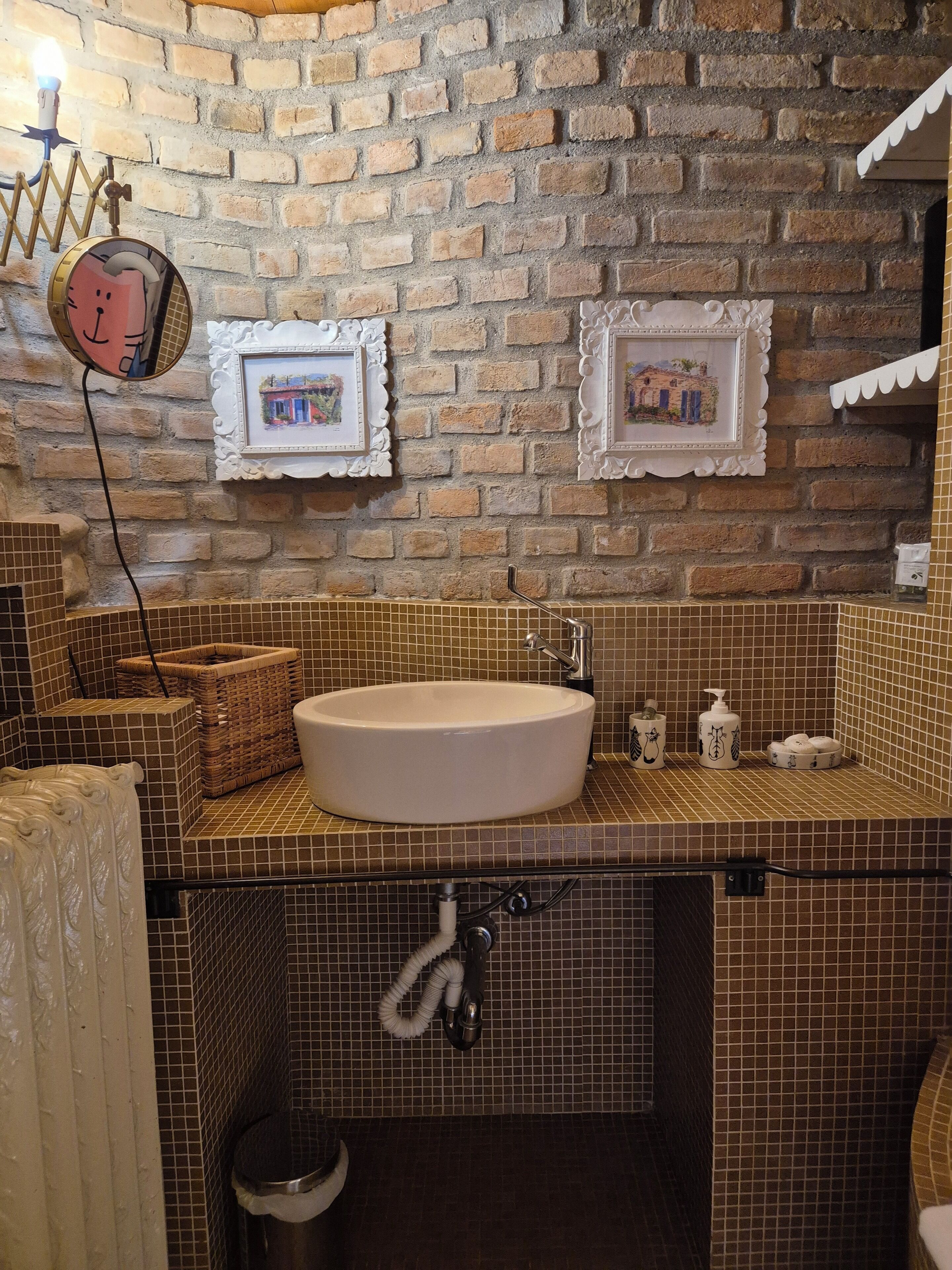 Ein Badezimmer mit Backsteinwand, einem runden Waschbecken und zwei gerahmten Bildern.