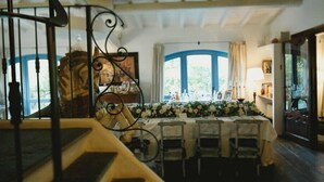 A dining area with a table set for four, surrounded by chairs, with a staircase in the foreground and a view of the outdoors through a window. - agriturismo il melo rosso   (Fortunago)