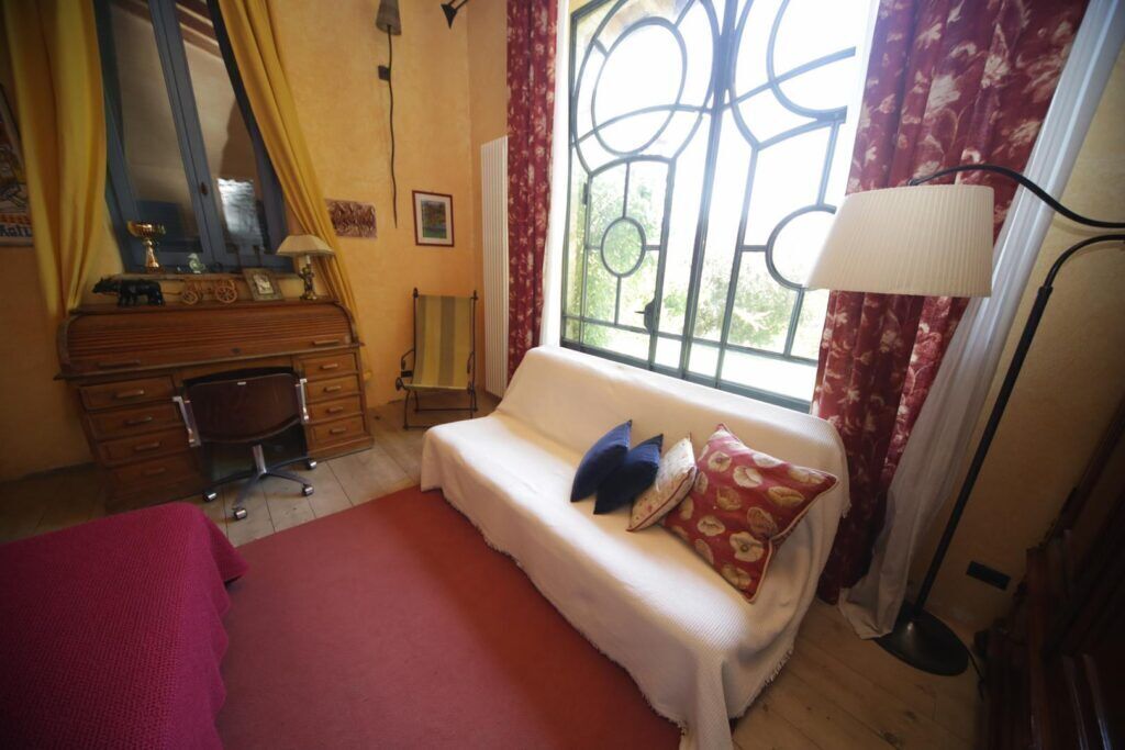 A bedroom with a bed, a sofa, a desk, and a window with curtains.