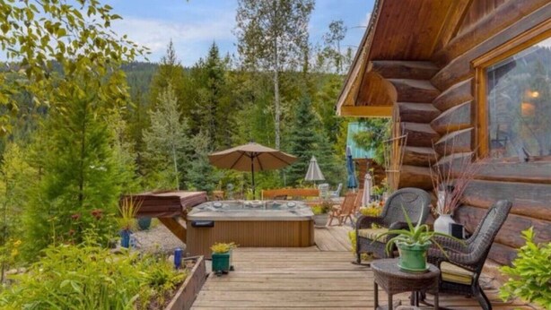 A log cabin with a hot tub, outdoor seating, and a deck surrounded by greenery. - Authentic lofted log cabin with hot tub (Kelowna)