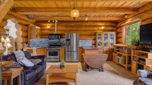 A log cabin interior with a kitchen, dining area, and living room. - Authentic lofted log cabin with hot tub (Kelowna)