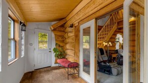 A log cabin interior with a wooden ceiling, a sliding glass door leading to a staircase, and a red bench by the door. - Authentic lofted log cabin with hot tub (Kelowna)