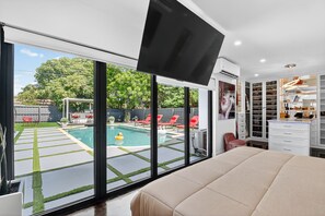 Un dormitorio moderno con una cama grande, un televisor montado en la pared y vistas a una piscina al aire libre.