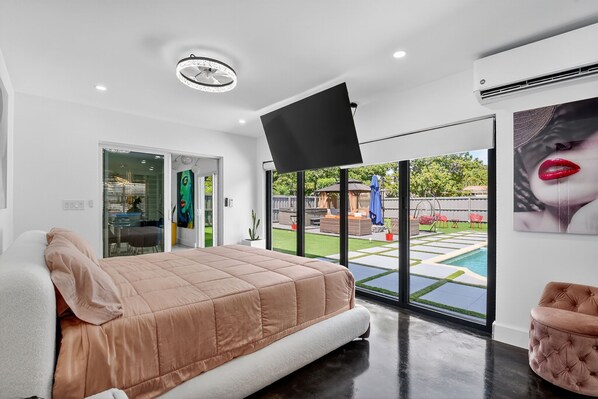 Un dormitorio moderno con una cama grande, un televisor de pantalla plana y vistas a una piscina y jardín.