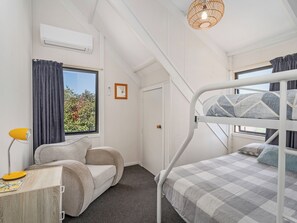 Una habitación con literas, un escritorio con lámpara, una ventana con cortinas y un equipo de aire acondicionado.