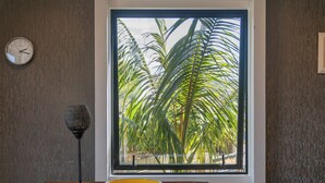 A dining area with a large window, a clock on the wall, and a table with a bowl and a lamp. - Spacious Family Getaway - Whangamata Holiday Home (Whangamata)