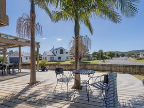 Una terraza de madera con una mesa y sillas, una zona cubierta y vistas a una casa y a la calle.