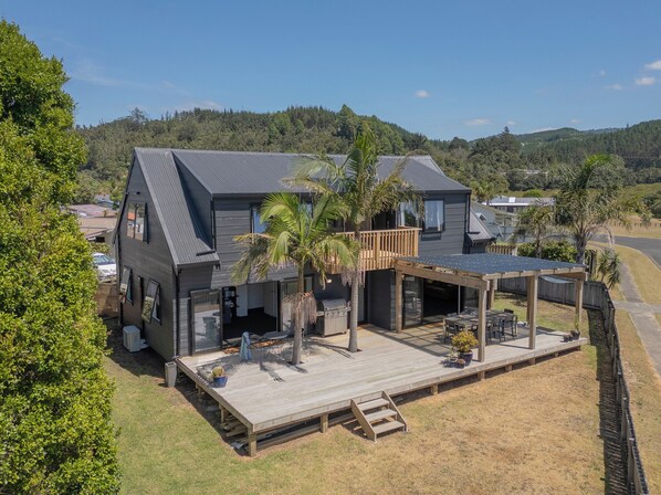 Una casa moderna de dos pisos con un porche cubierto, una terraza y vistas de las colinas circundantes.