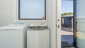 A compact laundry room with a washing machine, a dryer, and a sink. - Spacious Family Getaway - Whangamata Holiday Home (Whangamata)