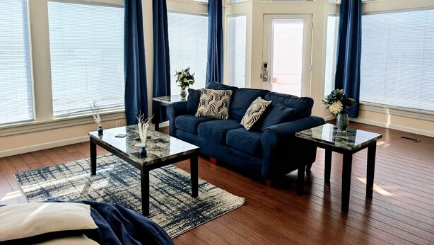 Un salon avec un canapé bleu foncé, deux tables basses et un tapis à motifs.