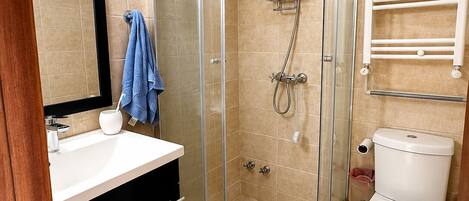 Un baño moderno con ducha de vidrio, lavamanos blanco y retrete.