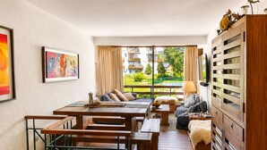 A room with a dining area, a sofa, a lamp, and a view of a pool and greenery.