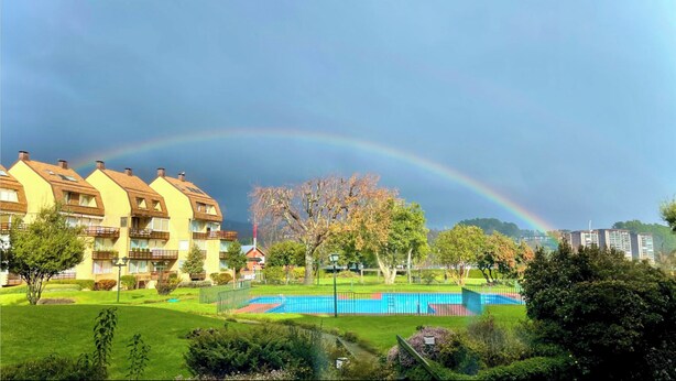 A residential area with a swimming pool, a rainbow, and a park with trees and a fence.