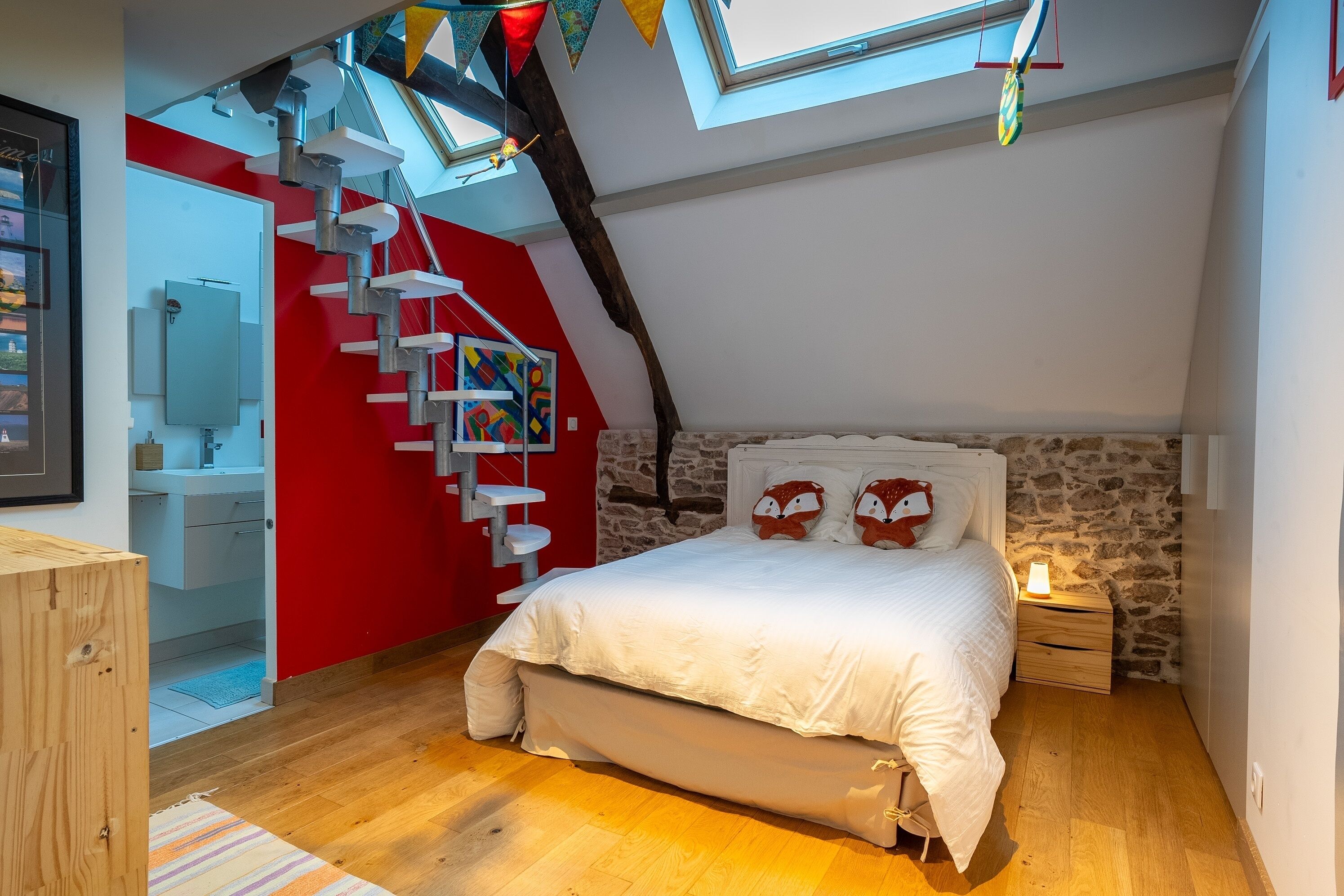 Ein Schlafzimmer mit schrägen Wänden, einem weißen Bett, einer Steinwand und einer roten Akzentwand.