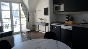A modern kitchen with a microwave, coffee machine, and dishwasher. There is a dining table with chairs, a small side table, and a window with curtains. - La plage du Trez - Charmant duplex avec vue mer (Benodet)
