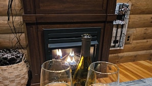 Ein Kamin mit Feuer, zwei Weingläser auf einem Holztablett und eine Weinflasche davor.
