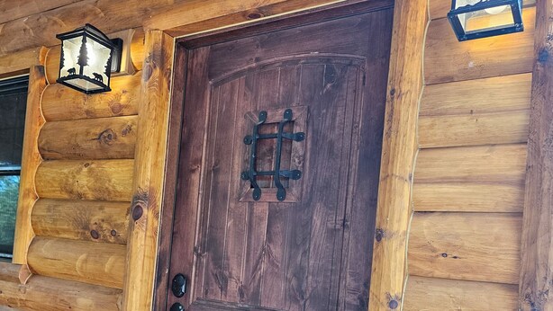 Eine Holzhütte mit einer dunkelbraunen Tür, die einen Metallriegel und ein Glasfenster aufweist.