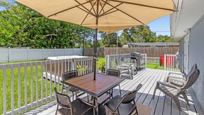 A wooden deck with a table and chairs under a large umbrella, surrounded by a white fence and greenery. - 4BR/3BR - Spacious Home 4 Minutes From Beach (Largo)