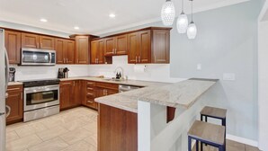 A modern kitchen with wooden cabinets, stainless steel appliances, and a marble countertop. - 4BR/3BR - Spacious Home 4 Minutes From Beach (Largo)