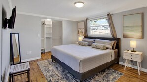 A bedroom with a large bed, a bedside table with a lamp, a wardrobe, and a window with curtains. - 4BR/3BR - Spacious Home 4 Minutes From Beach (Largo)