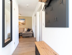 Un couloir avec un banc en bois, un canapé gris et un porte-manteau fixé au mur.