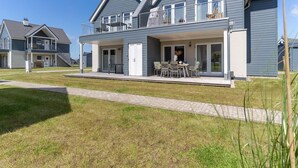 A two-story residential building with a balcony, a covered patio with outdoor seating, and a paved walkway. - Ferienwohnung in Busum (Büsum)