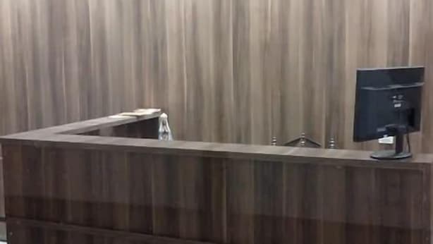 Un mostrador de recepción con detalles de madera, un monitor de computadora y una vitrina de vidrio.