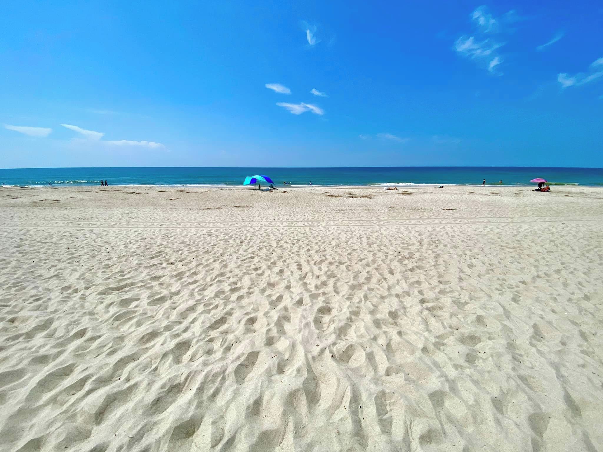 Una playa arenosa con cielo despejado y algunas personas a lo lejos.