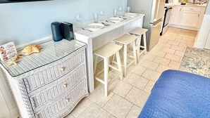A modern kitchen with white countertops, a built-in oven, and a dining area with stools.