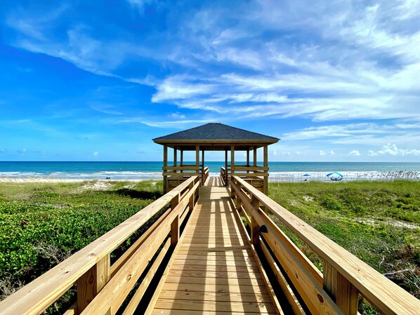 A wooden boardwalk leading to a beach pavilion with a view of the ocean.