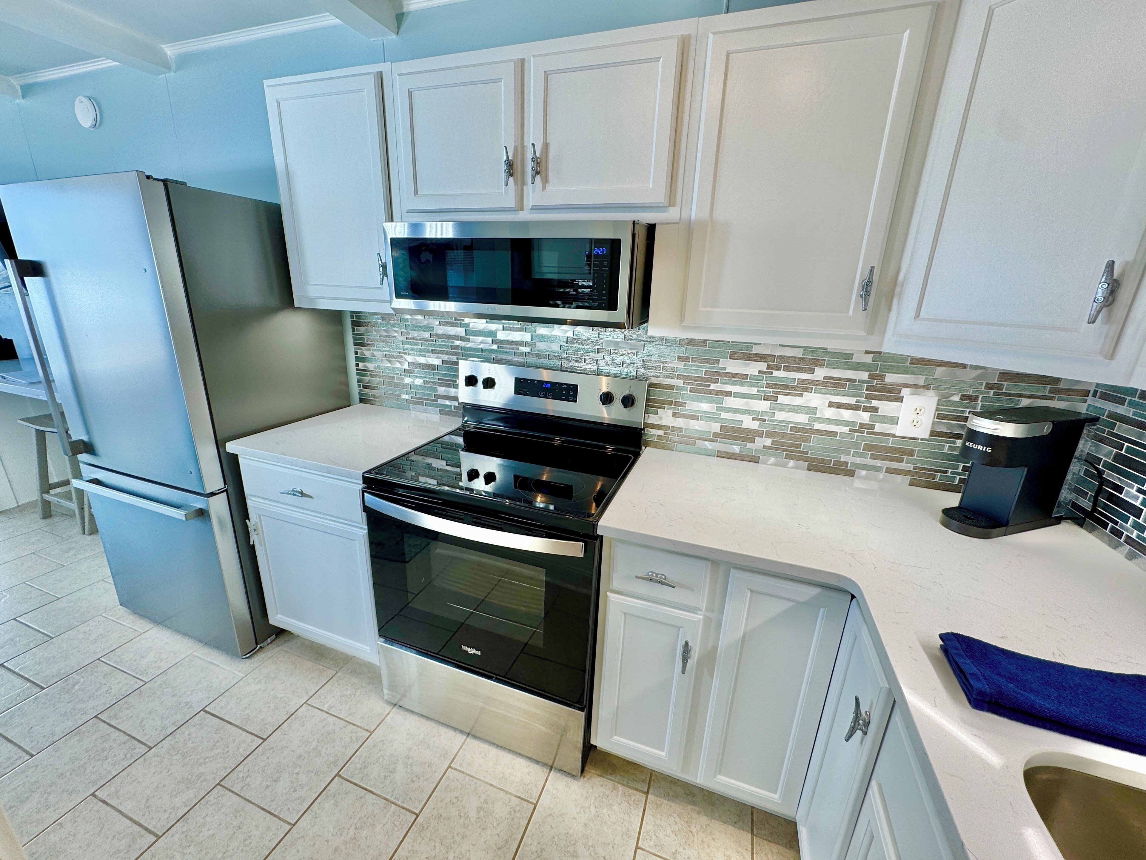 Una cocina moderna con armarios blancos, electrodomésticos de acero inoxidable, microondas, horno y cafetera.