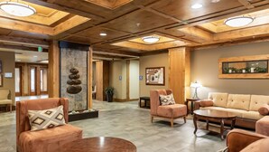 A lobby with wooden ceiling beams, a stone wall with a rock display, and a seating area with sofas and a round table. - Penthouse 2 Bedrm Suncadia Condo (Cle Elum)