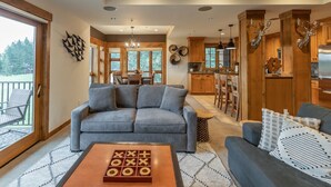 A modern living room with a grey sofa, a wooden coffee table, and a view of the kitchen and dining area. - Penthouse 2 Bedrm Suncadia Condo (Cle Elum)