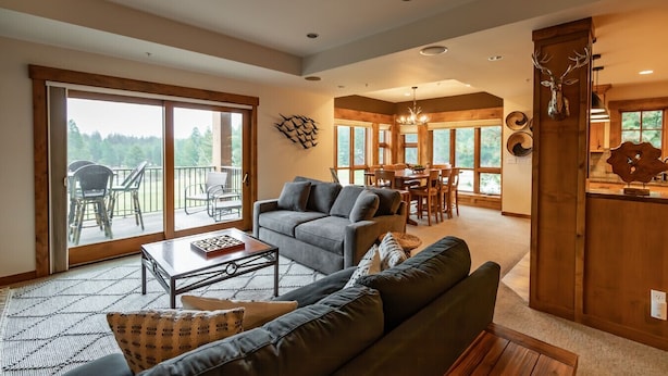 A spacious living room with a grey sofa, a coffee table, and a dining area with wooden furniture. - Penthouse 2 Bedrm Suncadia Condo (Cle Elum)