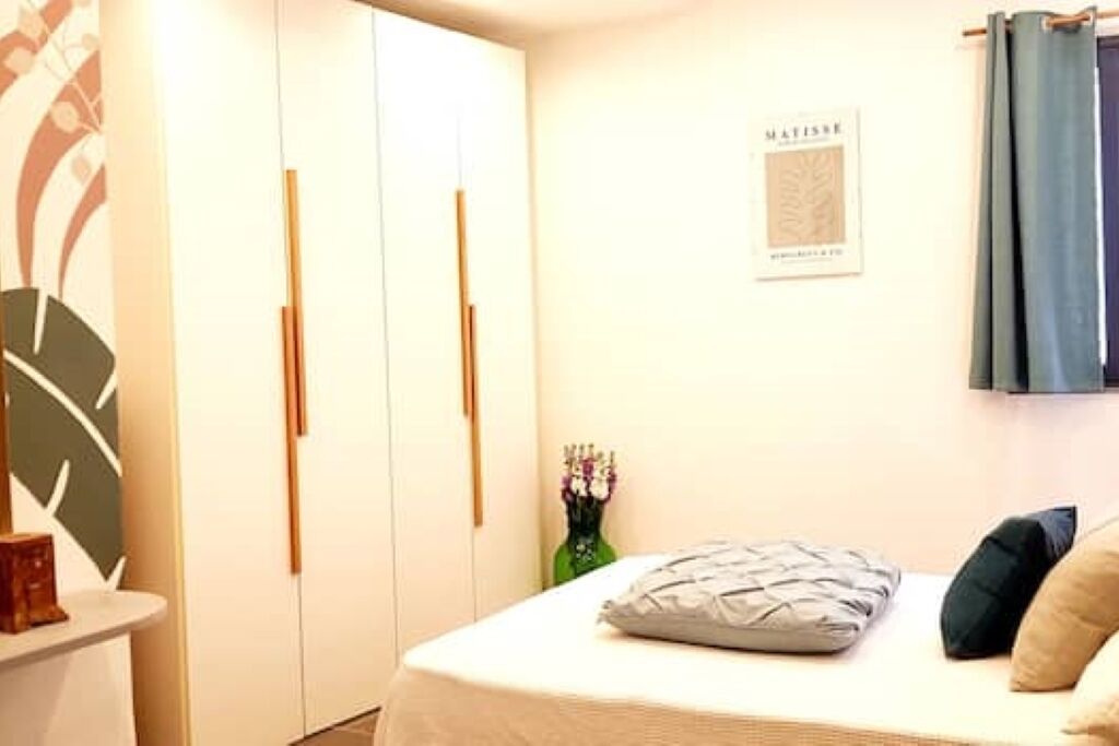A bedroom with a bed, a nightstand, a vase with flowers, a framed picture on the wall, and a wardrobe.