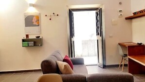 A living room with a sofa, a coffee table, a desk, and a door leading to an outdoor area.