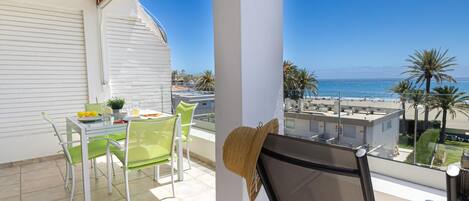 Ein Balkon mit Tisch und Stühlen, Blick auf den Strand und eine Palme.