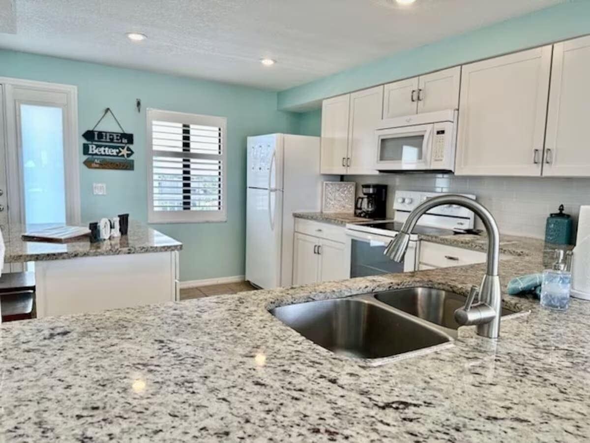 A kitchen with white cabinets, a granite countertop, stainless steel sink, and a microwave.